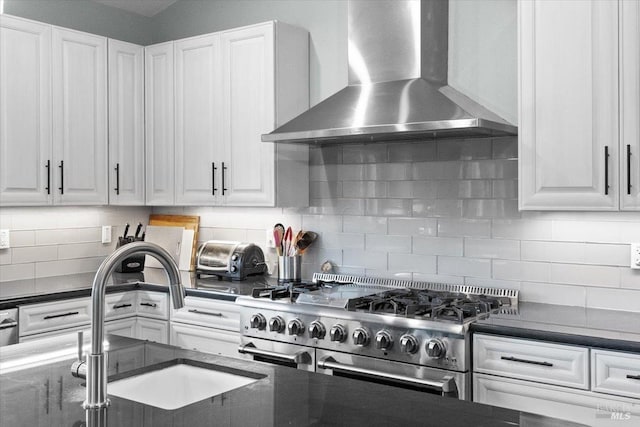 kitchen with decorative backsplash, range with two ovens, wall chimney exhaust hood, white cabinetry, and a sink