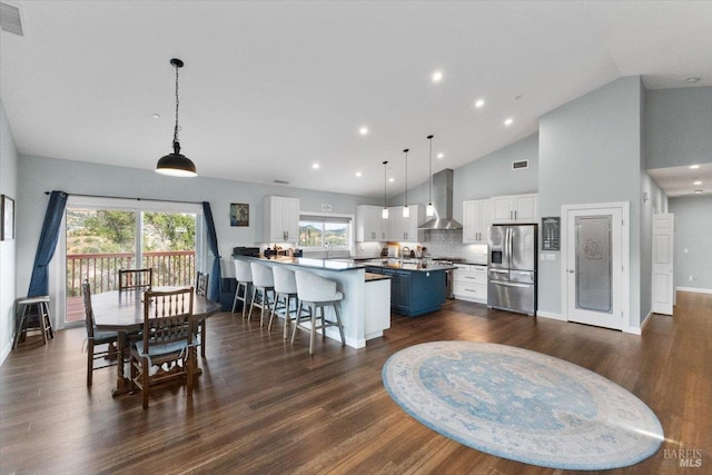 kitchen with a breakfast bar, dark wood-type flooring, white cabinetry, wall chimney range hood, and stainless steel fridge