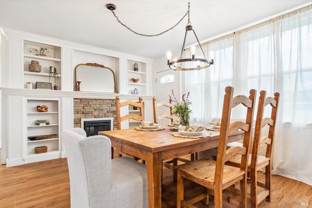 dining space featuring light hardwood / wood-style floors, a stone fireplace, and a notable chandelier