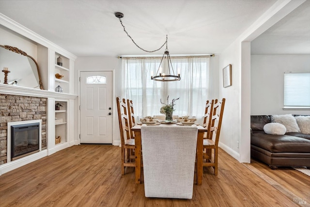 dining space with a chandelier, built in shelves, light hardwood / wood-style floors, and a stone fireplace