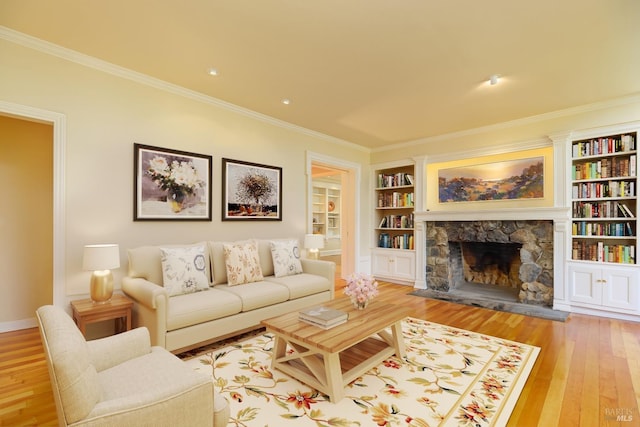 living room featuring built in shelves, a stone fireplace, ornamental molding, and light hardwood / wood-style flooring