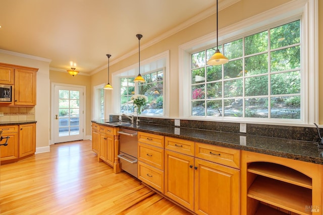 kitchen featuring hanging light fixtures, stainless steel microwave, ornamental molding, light hardwood / wood-style floors, and dark stone counters