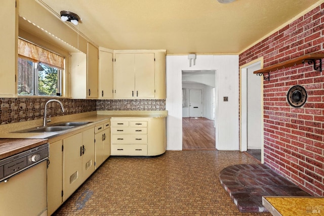 kitchen with dishwasher, brick wall, light countertops, cream cabinetry, and a sink