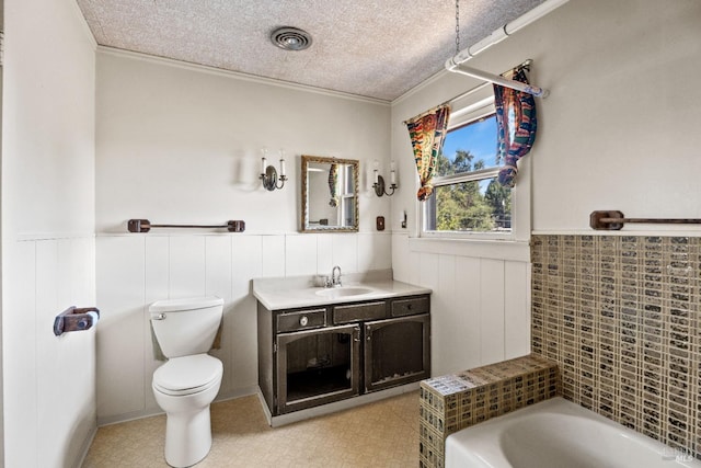 bathroom featuring a washtub, a wainscoted wall, a textured ceiling, and toilet