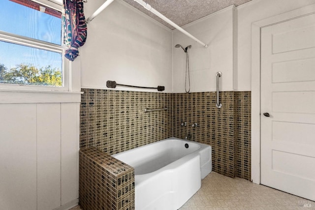 full bathroom with a wainscoted wall, tile walls, a textured ceiling,  shower combination, and tile patterned floors