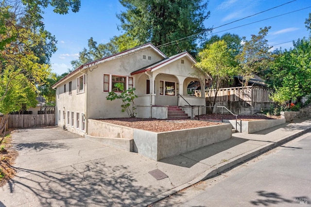 view of front of house featuring driveway, fence, a porch, and stucco siding