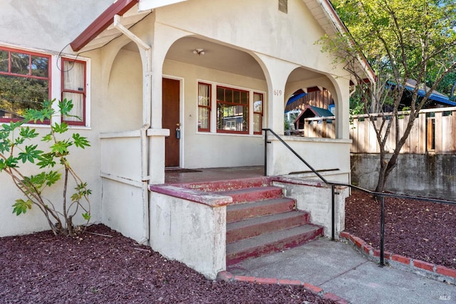 view of exterior entry featuring covered porch, fence, and stucco siding