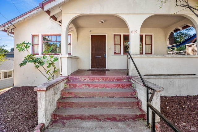 doorway to property with covered porch and stucco siding