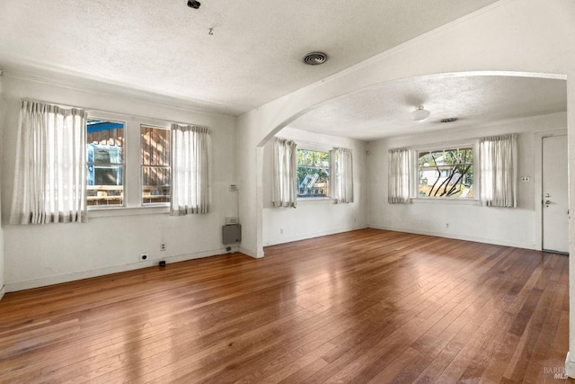 empty room with arched walkways, visible vents, a textured ceiling, and hardwood / wood-style flooring