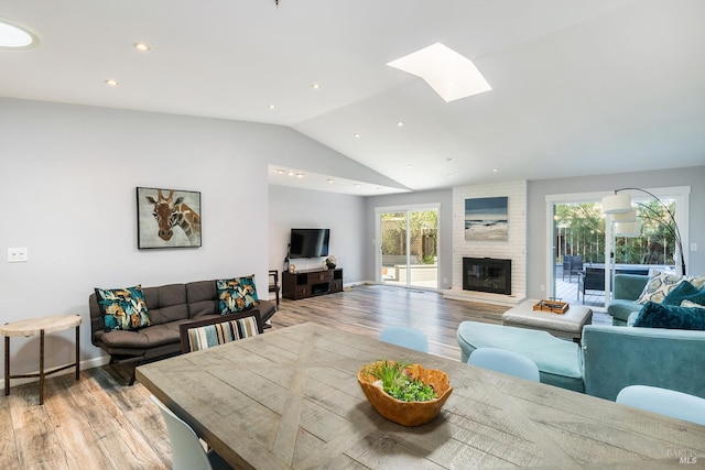 interior space with lofted ceiling with skylight, light hardwood / wood-style floors, and a large fireplace