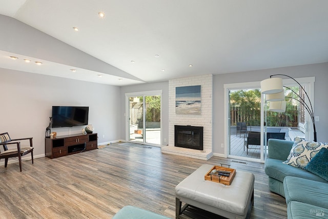 living room with wood-type flooring, vaulted ceiling, and a brick fireplace