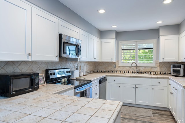 kitchen featuring tasteful backsplash, appliances with stainless steel finishes, sink, tile countertops, and white cabinets
