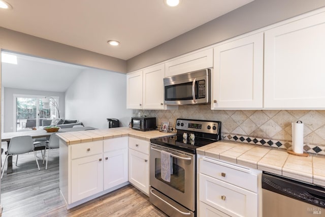 kitchen with white cabinetry, kitchen peninsula, stainless steel appliances, and tile counters