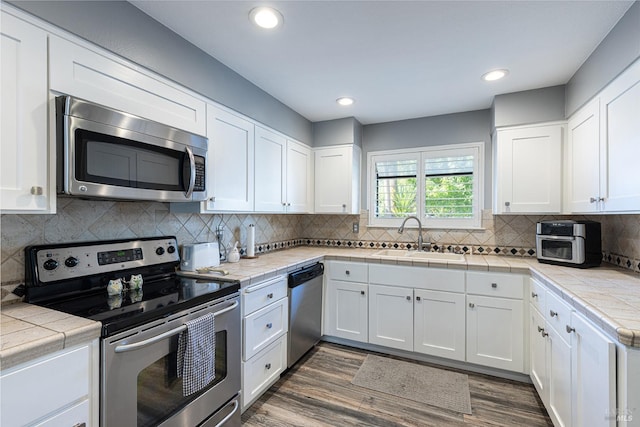 kitchen featuring sink, tile countertops, dark hardwood / wood-style flooring, white cabinetry, and stainless steel appliances