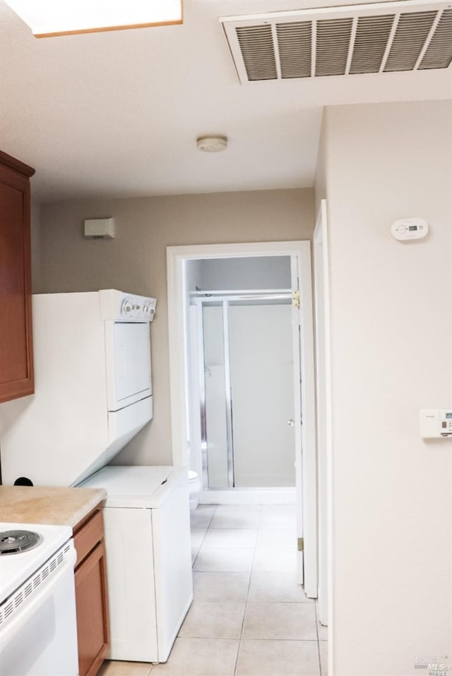 kitchen featuring light tile patterned floors, electric stove, and stacked washer / drying machine