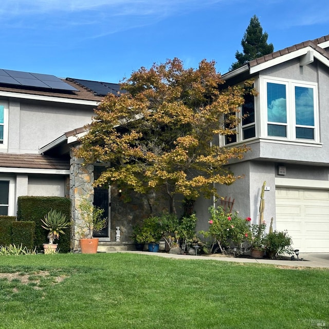 view of front of property featuring a garage, solar panels, and a front yard