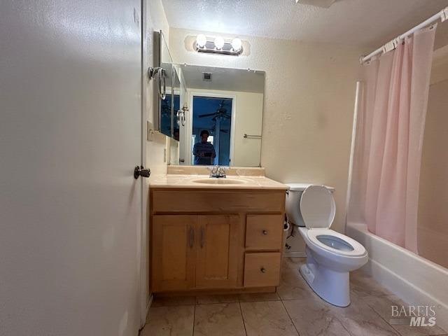 full bathroom featuring shower / bath combo, a textured ceiling, vanity, and toilet