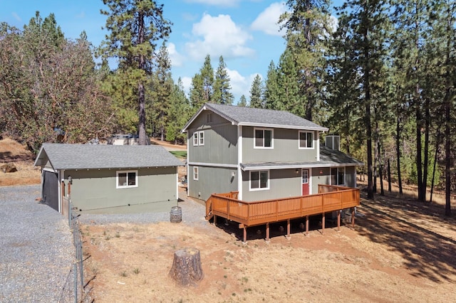 back of property featuring driveway, a shingled roof, an outdoor structure, and a wooden deck