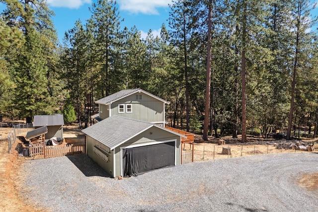 view of front of home with an outbuilding, a shingled roof, gravel driveway, and fence