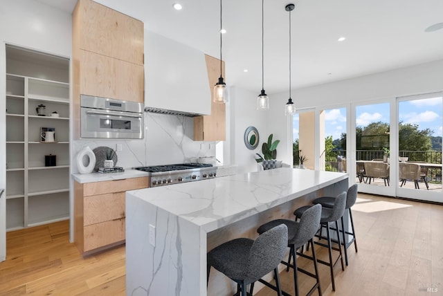 kitchen with decorative light fixtures, light wood-type flooring, stainless steel appliances, and light stone counters