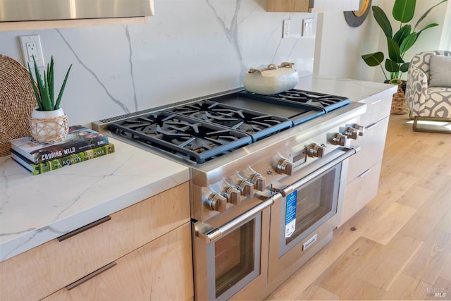 kitchen featuring light stone countertops, light brown cabinets, light hardwood / wood-style flooring, and double oven range