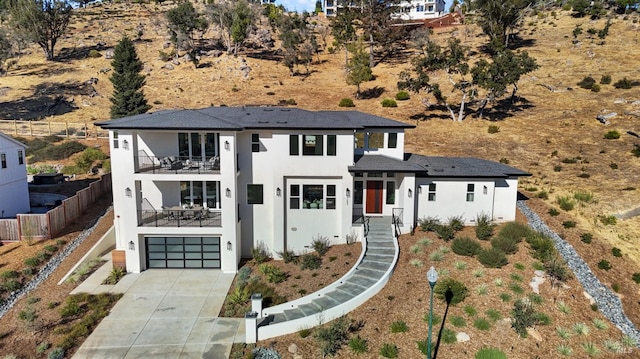 view of front of home featuring an attached garage, a balcony, fence, concrete driveway, and stucco siding