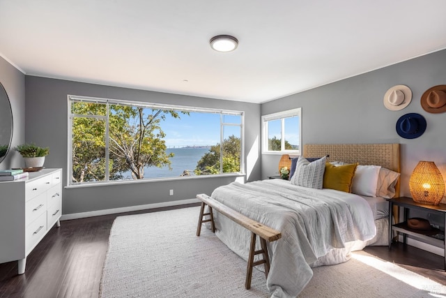 bedroom with dark wood-style floors, a water view, and baseboards