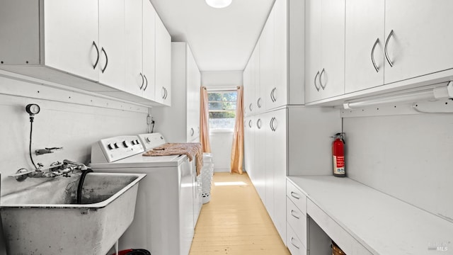 clothes washing area with cabinets, sink, light hardwood / wood-style floors, and washing machine and dryer