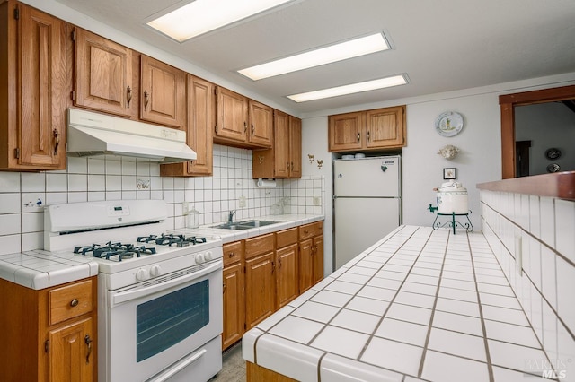 kitchen with light tile patterned floors, sink, white appliances, backsplash, and tile counters