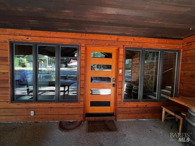 doorway featuring a healthy amount of sunlight, wooden ceiling, carpet floors, and wood walls