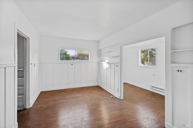 empty room with built in shelves, dark hardwood / wood-style flooring, and a baseboard heating unit