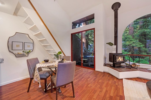 dining space with high vaulted ceiling, a wood stove, and hardwood / wood-style flooring