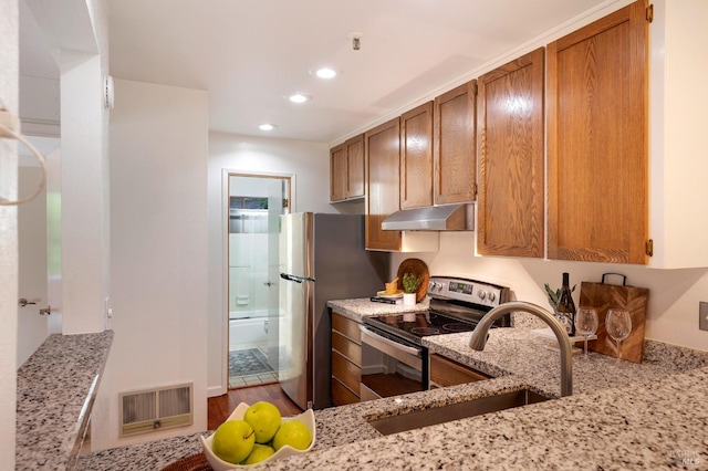 kitchen with appliances with stainless steel finishes, wood-type flooring, sink, and light stone counters