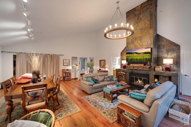 living room with track lighting, a high ceiling, an inviting chandelier, a fireplace, and hardwood / wood-style floors