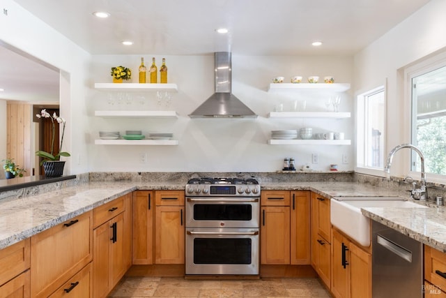 kitchen with wall chimney range hood, open shelves, light stone countertops, appliances with stainless steel finishes, and a sink