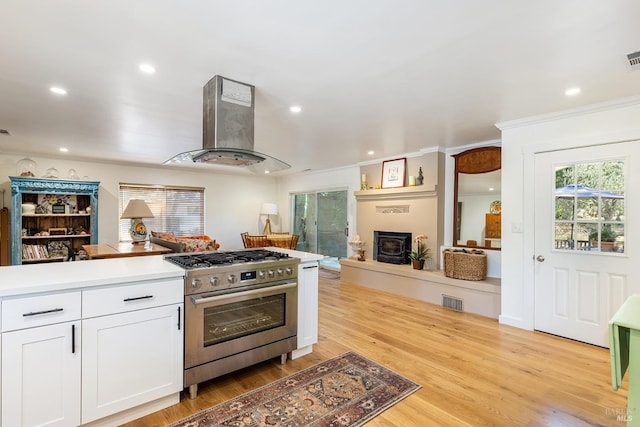 kitchen featuring white cabinets, wall chimney exhaust hood, open floor plan, stainless steel range with gas cooktop, and a fireplace