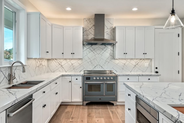 kitchen with appliances with stainless steel finishes, sink, wall chimney exhaust hood, pendant lighting, and white cabinets