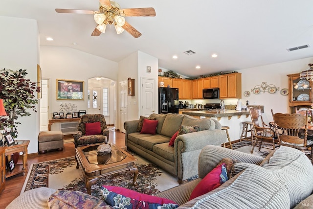 living room featuring arched walkways, visible vents, lofted ceiling, and wood finished floors