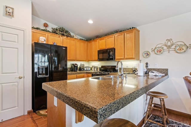 kitchen with lofted ceiling, a peninsula, a breakfast bar, light wood-style floors, and black appliances