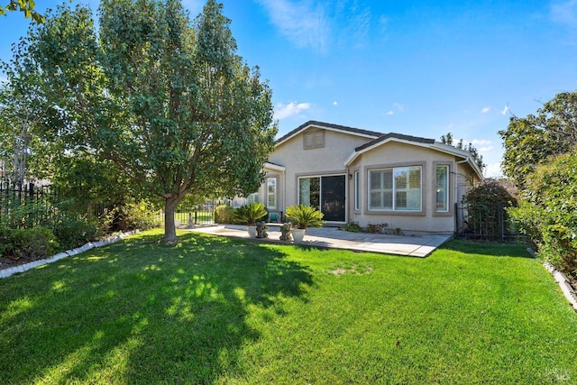 rear view of house featuring a yard, fence, and stucco siding