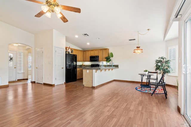 kitchen with arched walkways, dark countertops, vaulted ceiling, a peninsula, and black appliances