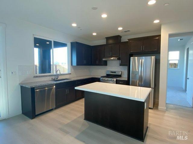 kitchen with decorative backsplash, light wood-type flooring, stainless steel appliances, sink, and a center island