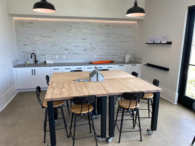 kitchen with a kitchen bar, sink, white cabinetry, hanging light fixtures, and butcher block counters