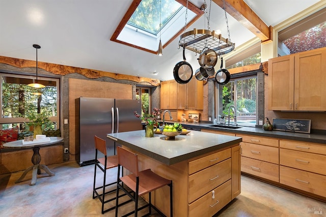 kitchen featuring vaulted ceiling with skylight, sink, an island with sink, hanging light fixtures, and stainless steel fridge