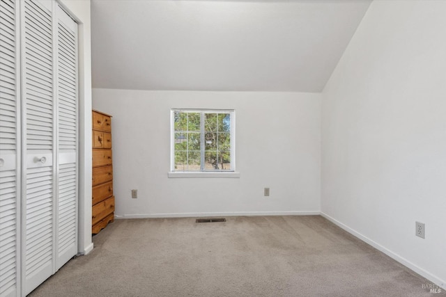 unfurnished bedroom featuring lofted ceiling, light carpet, and a closet