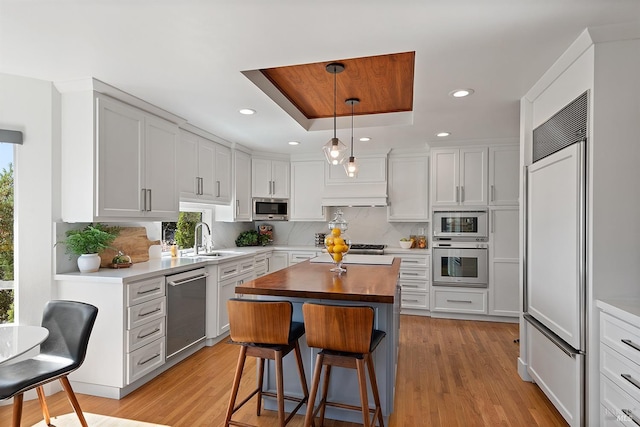 kitchen featuring sink, white cabinetry, built in appliances, decorative light fixtures, and a tray ceiling