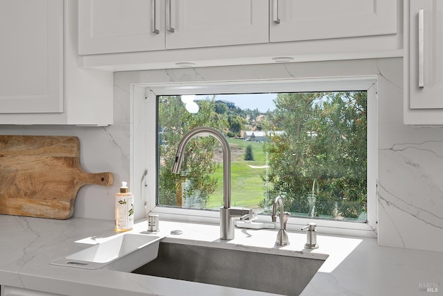 room details featuring white cabinetry, light stone countertops, and sink