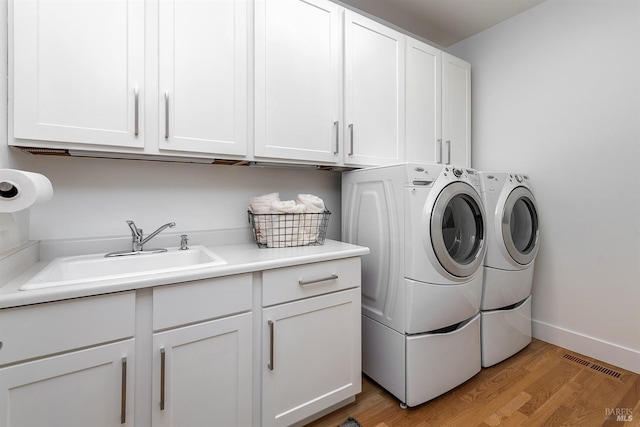 laundry area featuring cabinets, separate washer and dryer, sink, and light hardwood / wood-style flooring