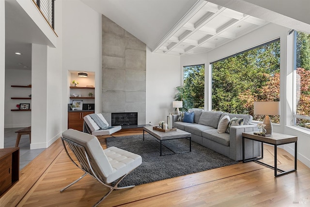 living room with a towering ceiling, beam ceiling, coffered ceiling, light hardwood / wood-style floors, and a tiled fireplace