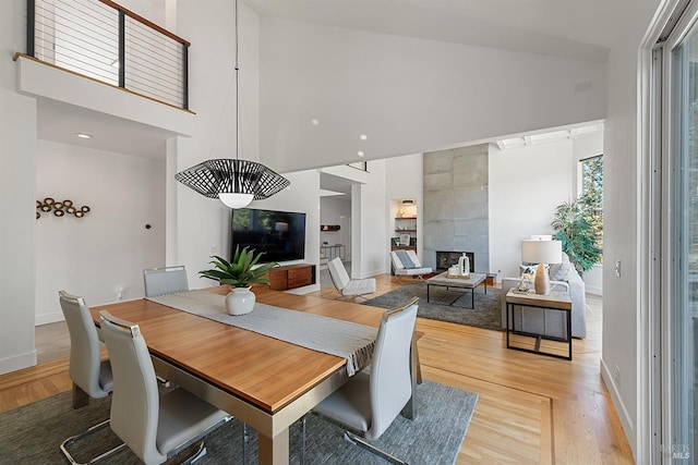 dining room with a tiled fireplace, a towering ceiling, and light wood-type flooring